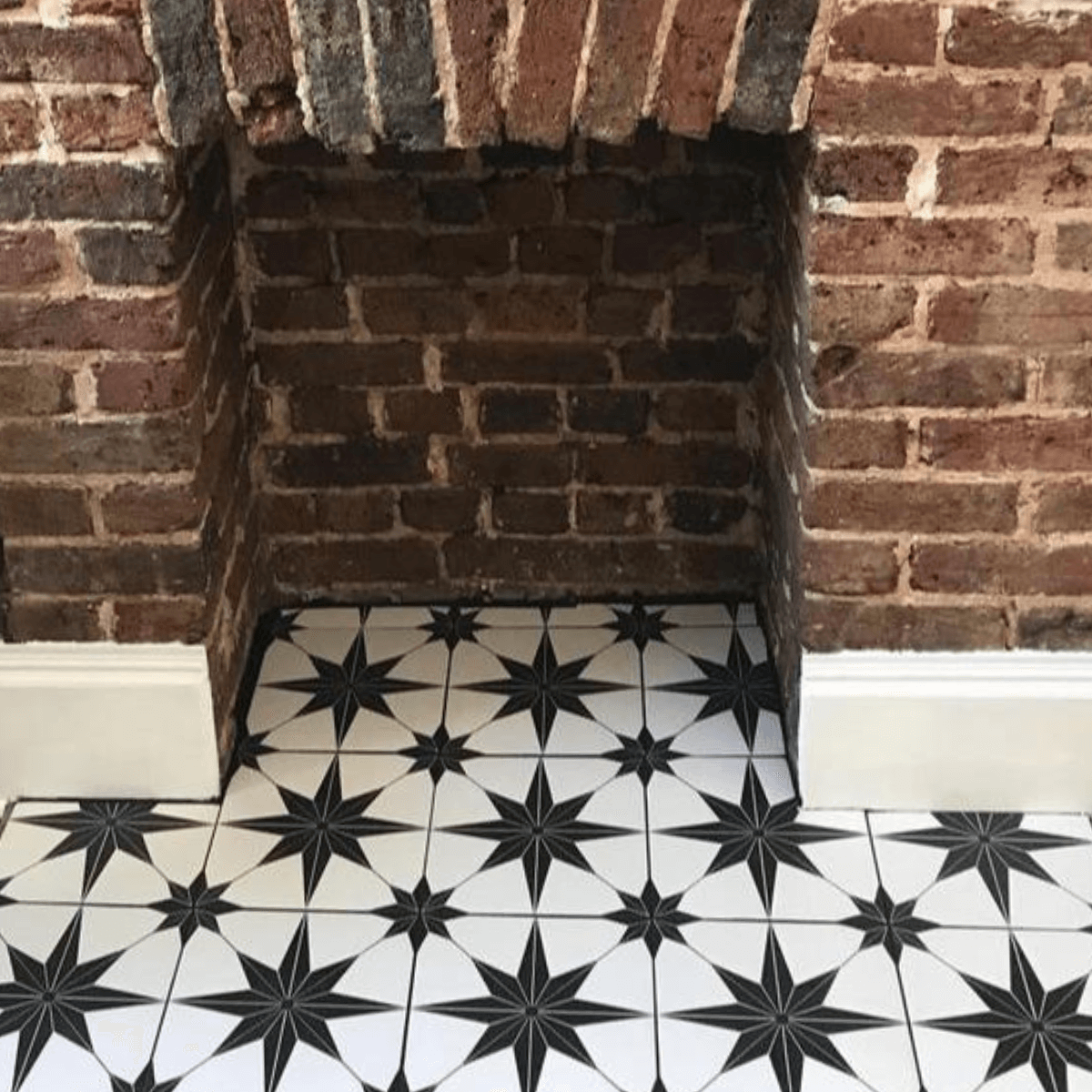 Lyra black star patterned tile laid in a hearth of an empty red brick fireplace