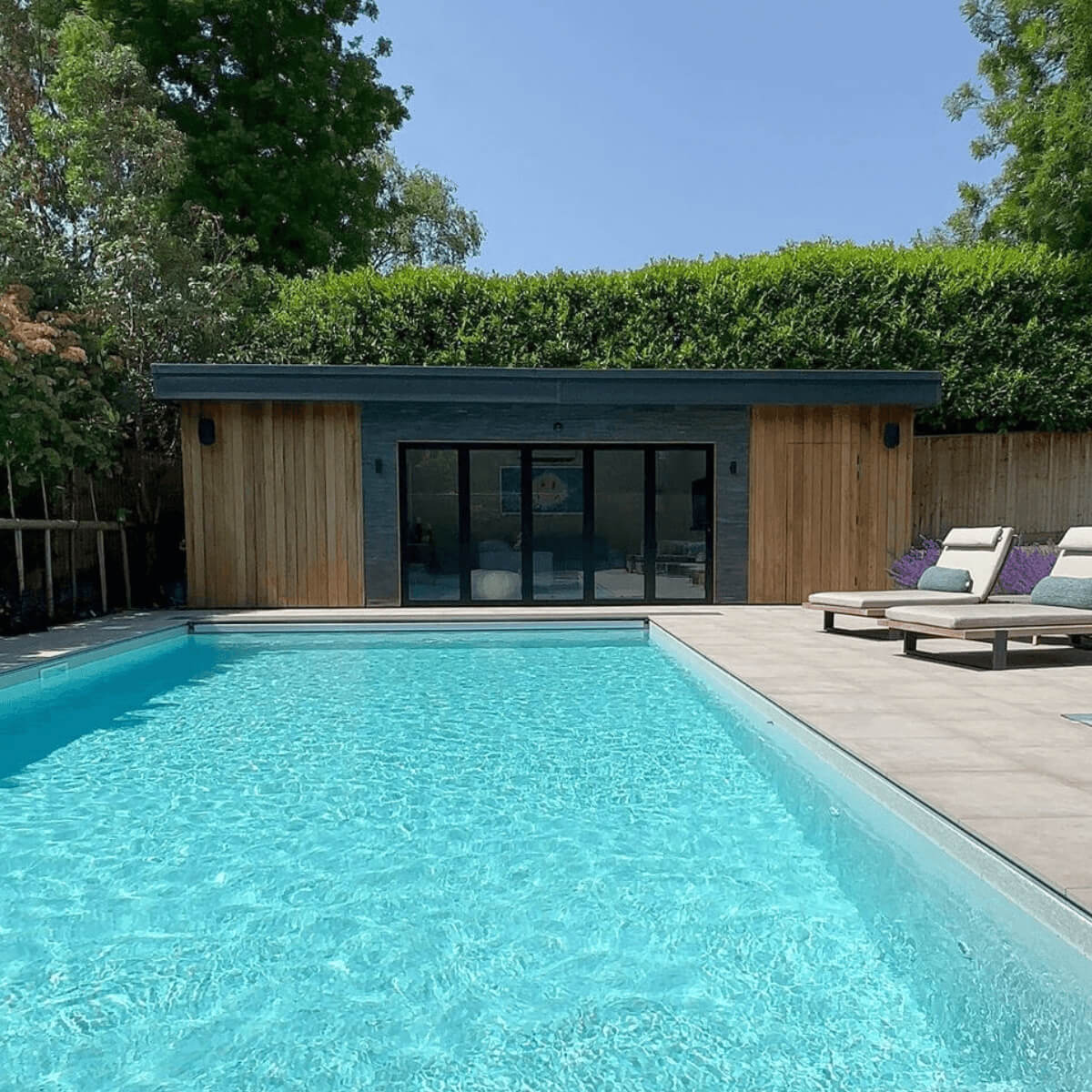 turquoise outdoor pool with two day beds and pool room with bi-folding anthracite doors and black split face stone to the front